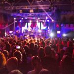Silhouettes crowd in front of brightly lit stage